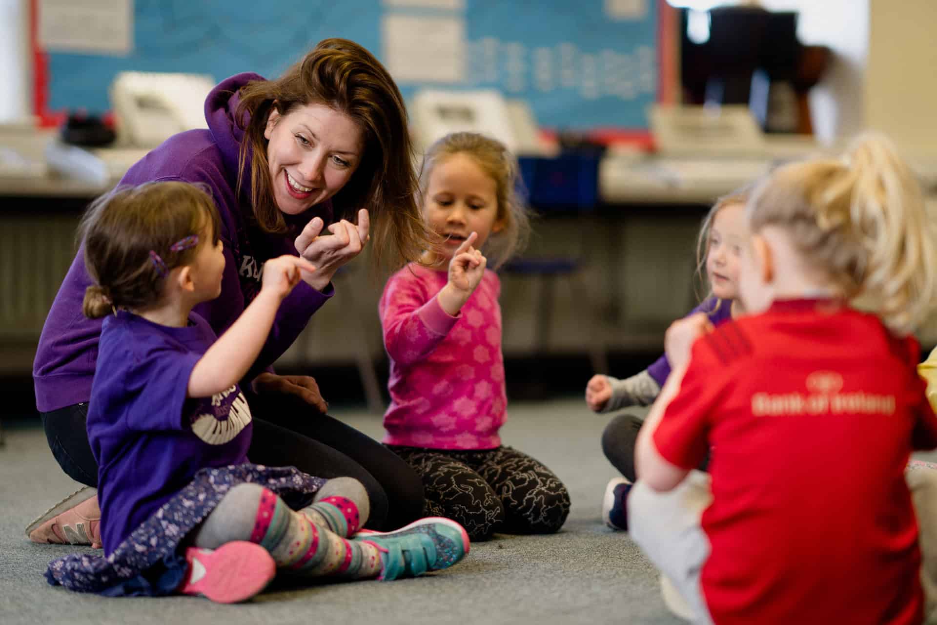Eine Lehrerin und Kinder spielen gemeinsam ein Fingerspiel.
